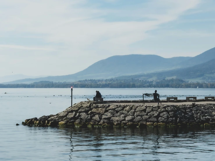 two people sit at the edge of a lake