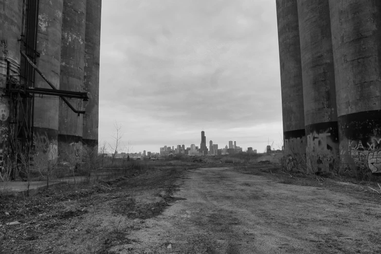 black and white pograph of dirt street with urban skyline in background