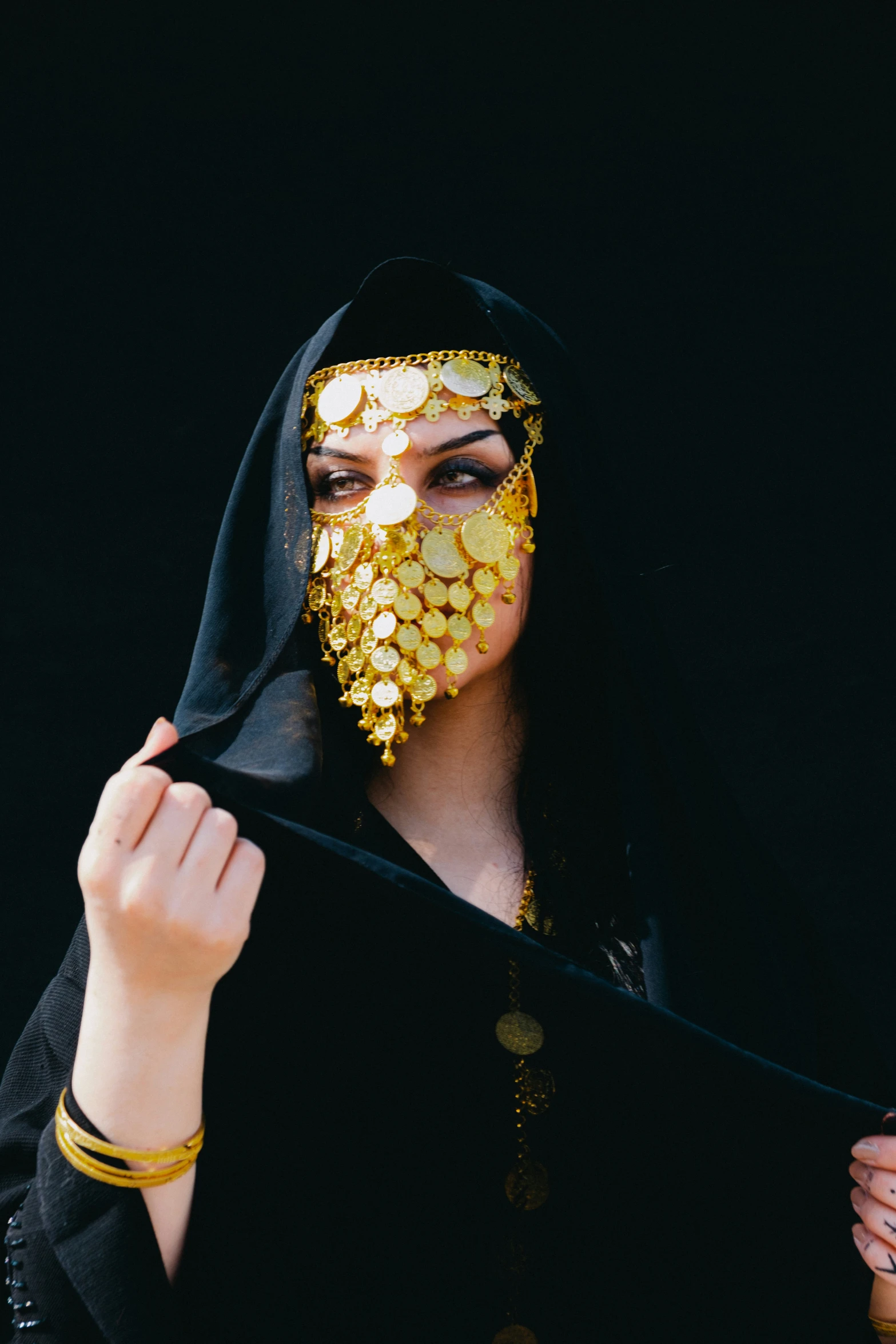 a woman in black hood and face covering with gold coins