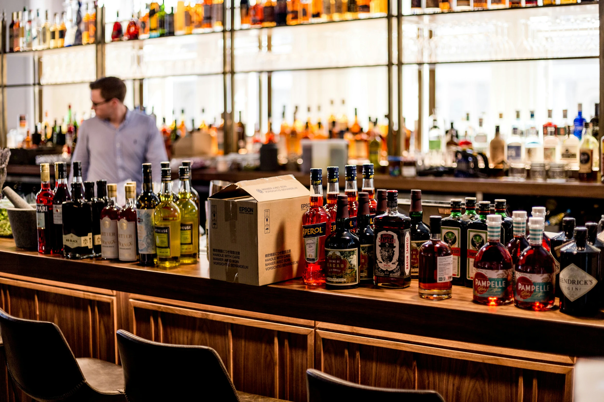 man standing behind the bar with various alcoholic bottles