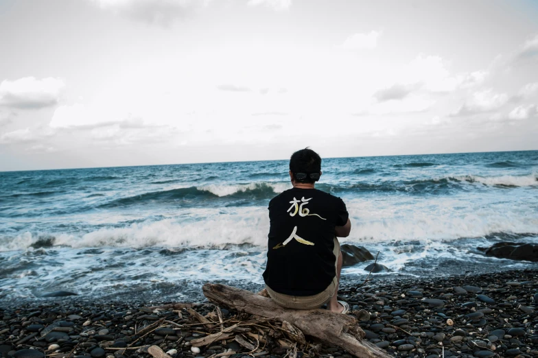 a man that is sitting on the rocks by the ocean