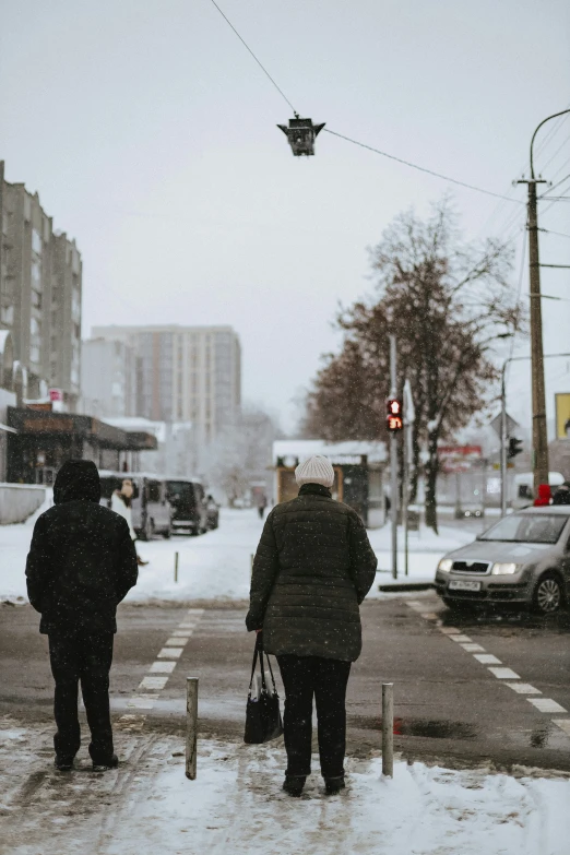 a street scene with two people crossing the street in the snow