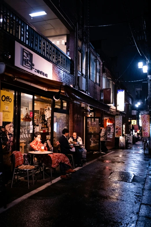 people sitting at tables in the rain on the street
