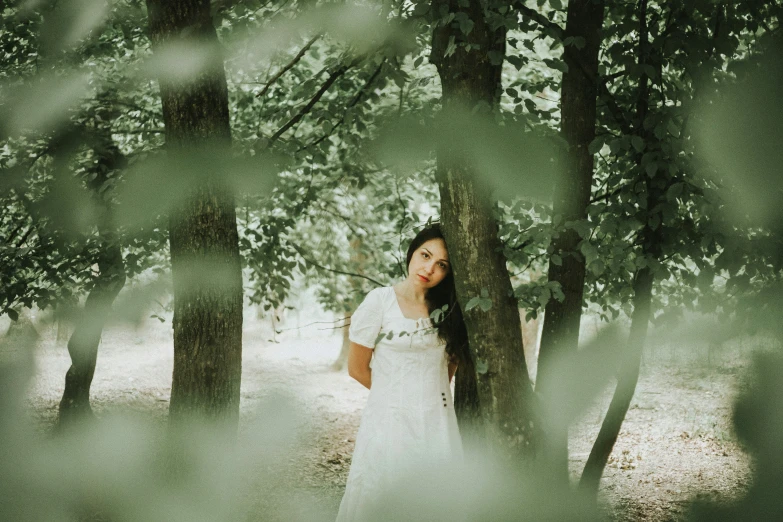 woman standing in a wooded area wearing a white dress