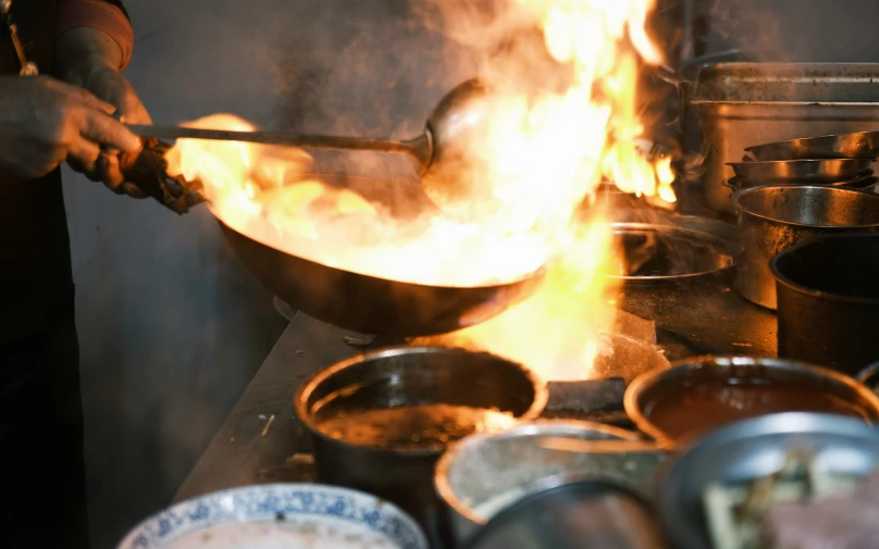 a person stirring a wok on fire with pots and pans surrounding