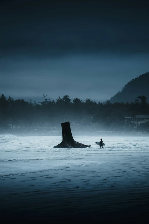 surfer carrying his surfboard into the ocean in heavy fog