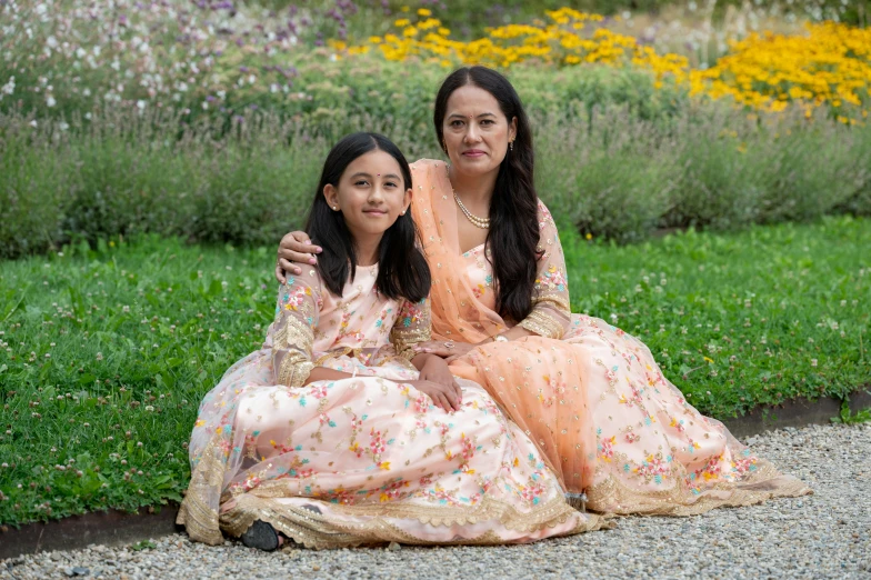 a couple of women sitting next to each other on top of grass