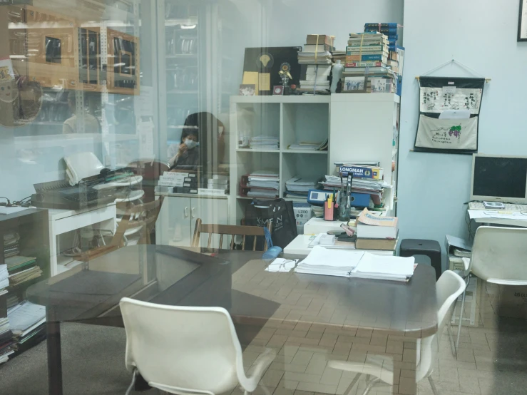 a view of a messy desk and book shelves from inside a window