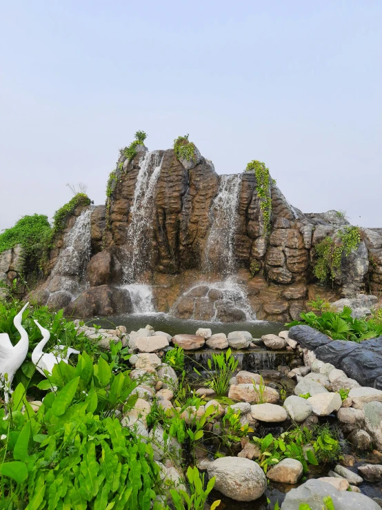 a bird statue sits on the ground next to a rocky hill