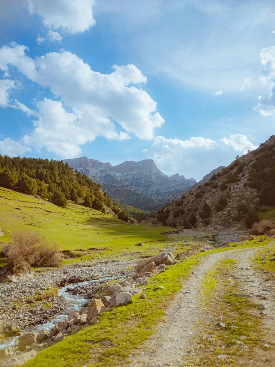 a dirt road passes through mountains that have green grass and water