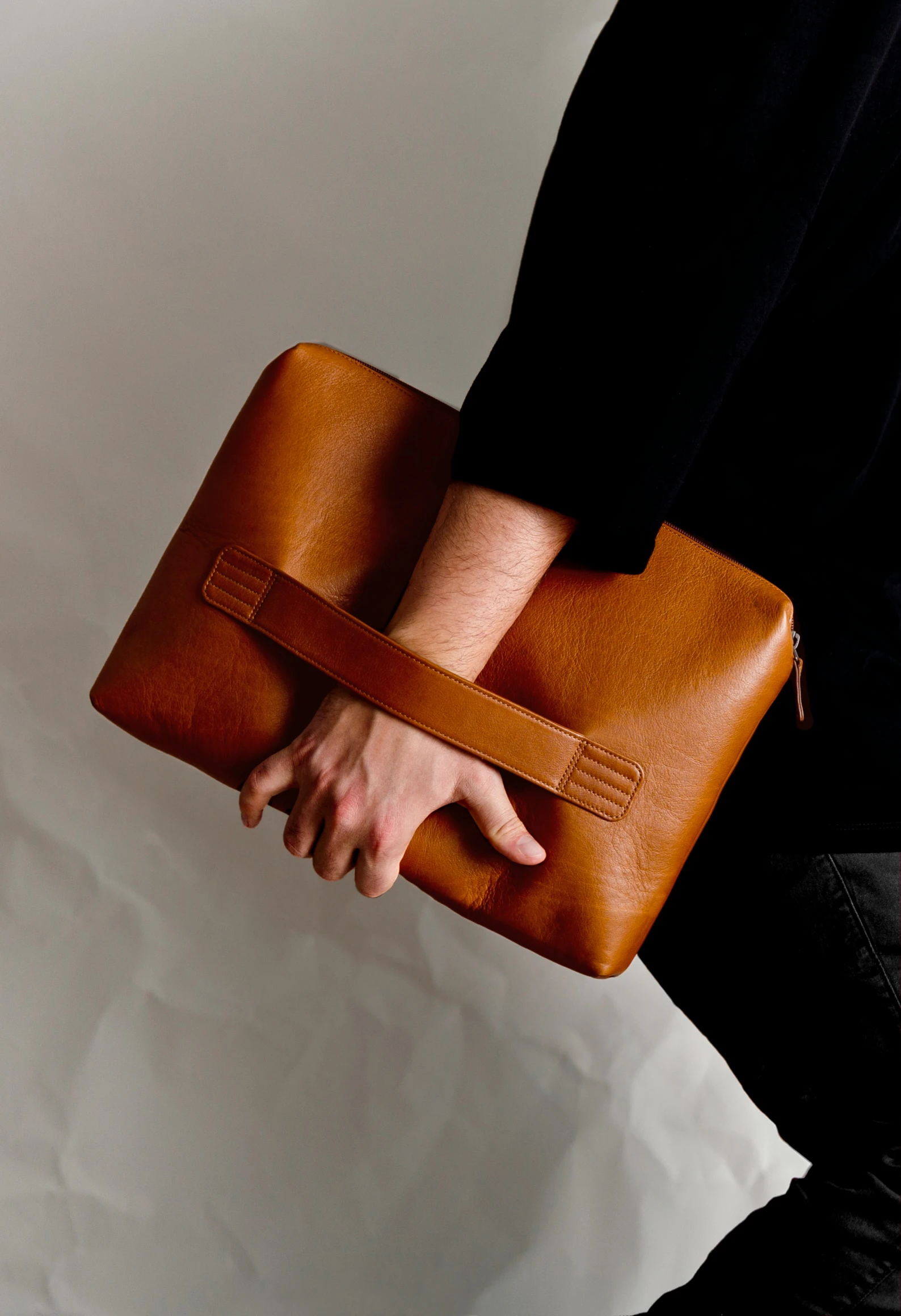 person holding a small brown briefcase against a white backdrop