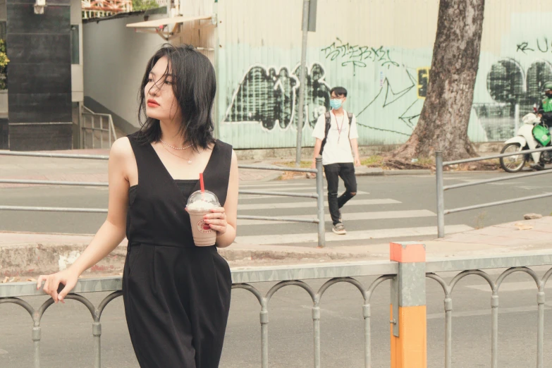 a young woman is standing next to a fence with an iced beverage