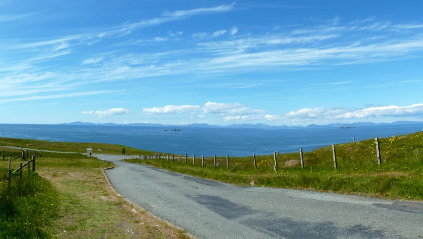 a paved road in a grassy area with a view of the ocean in the background