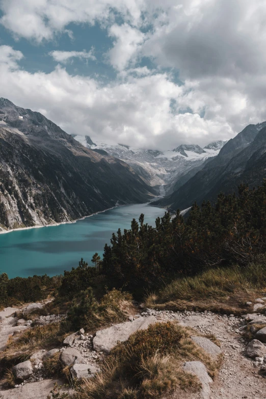 an unpaved rocky trail extends out into a lake and mountainous area