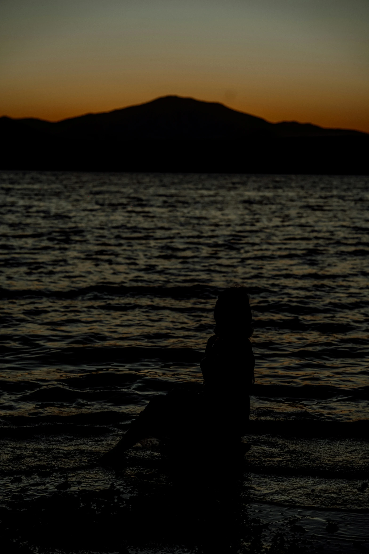 a person sitting on a surfboard with the ocean at sunset