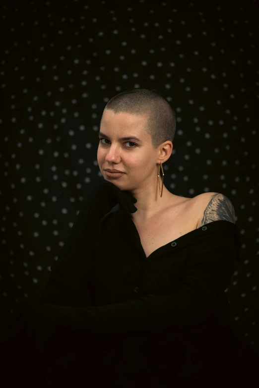 a young woman with shaved head and piercings in a black dress