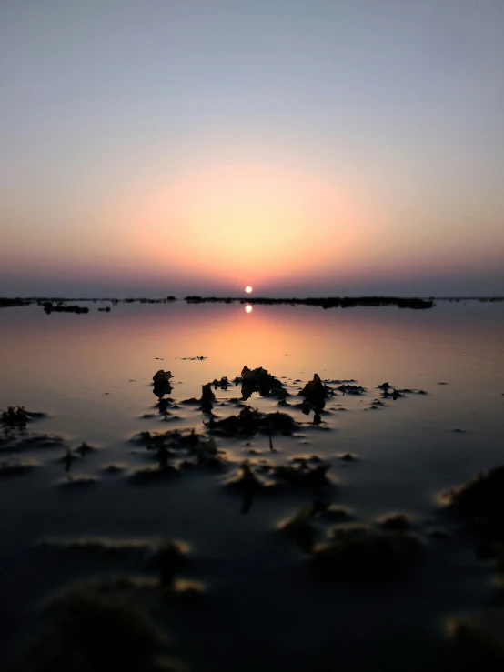 the sun is setting over the water on a beach