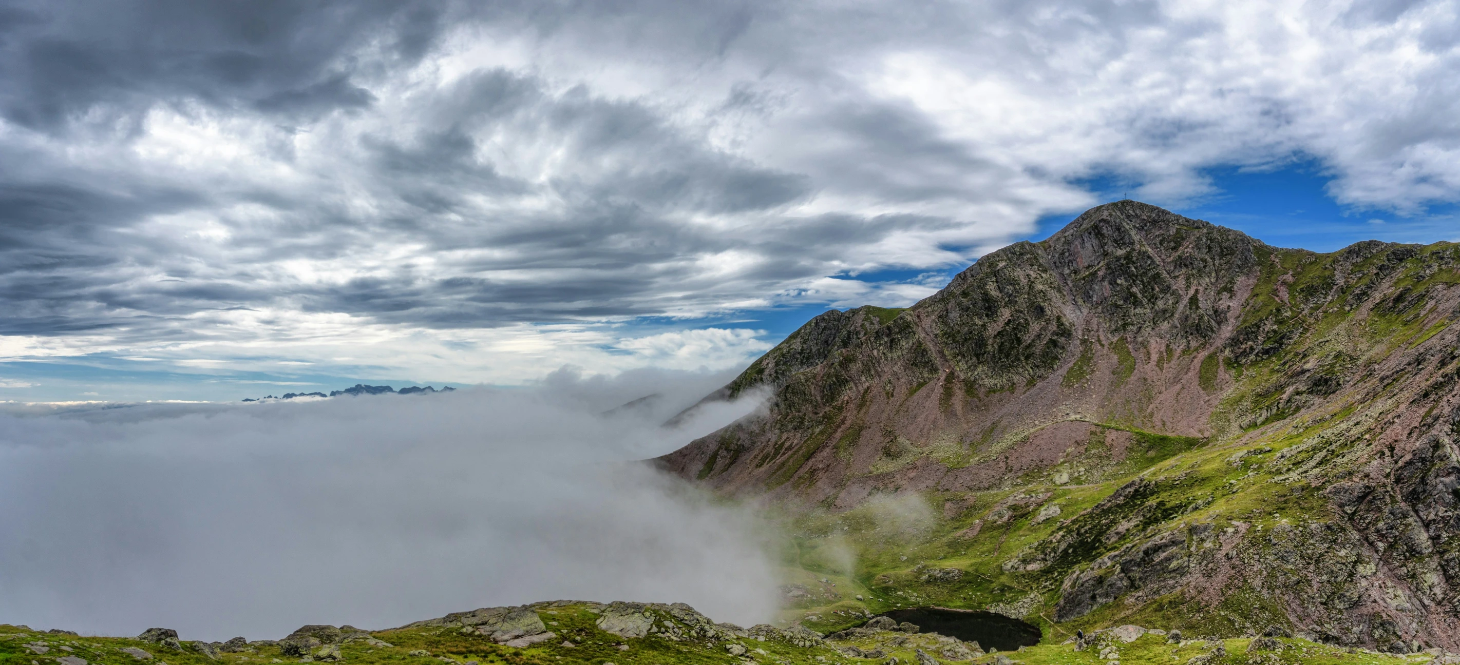 a very high mountain side with a bunch of clouds in the background