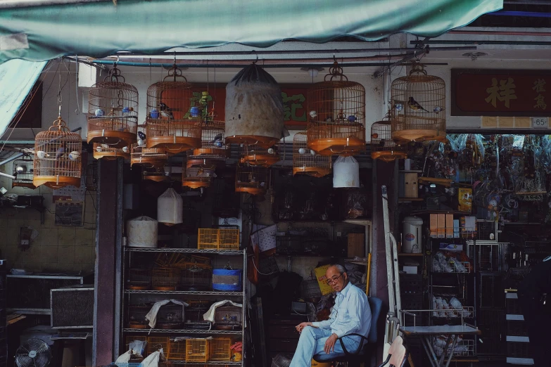 a man sits outside his stall selling many cages