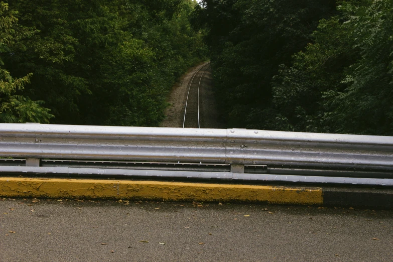 a gray rail that goes down from the road and through the forest