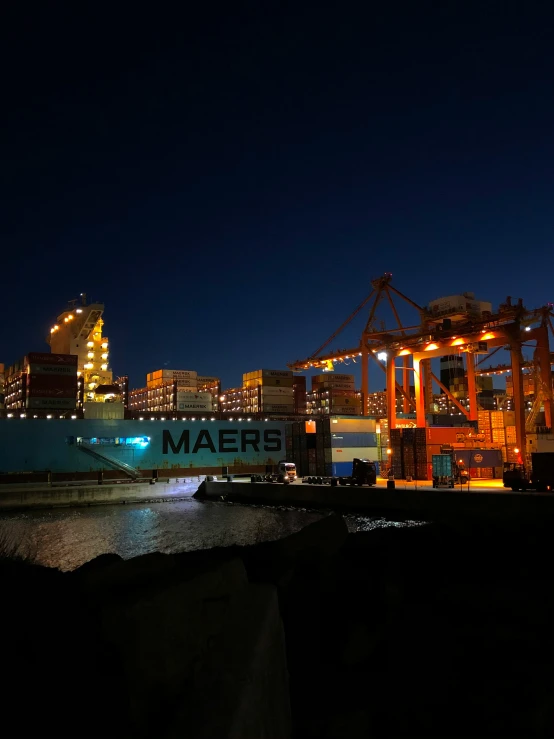 a cargo ship with cranes in the background at night