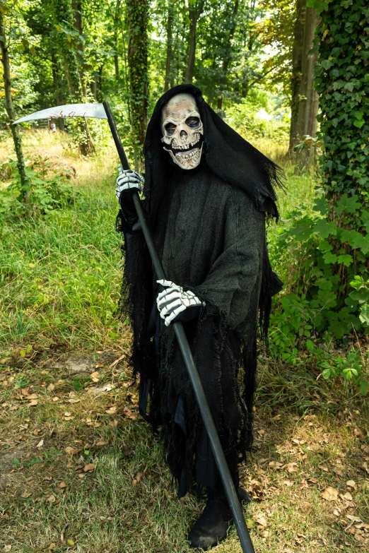 a man in a black zombie costume holding a staff and wearing a large long black grime