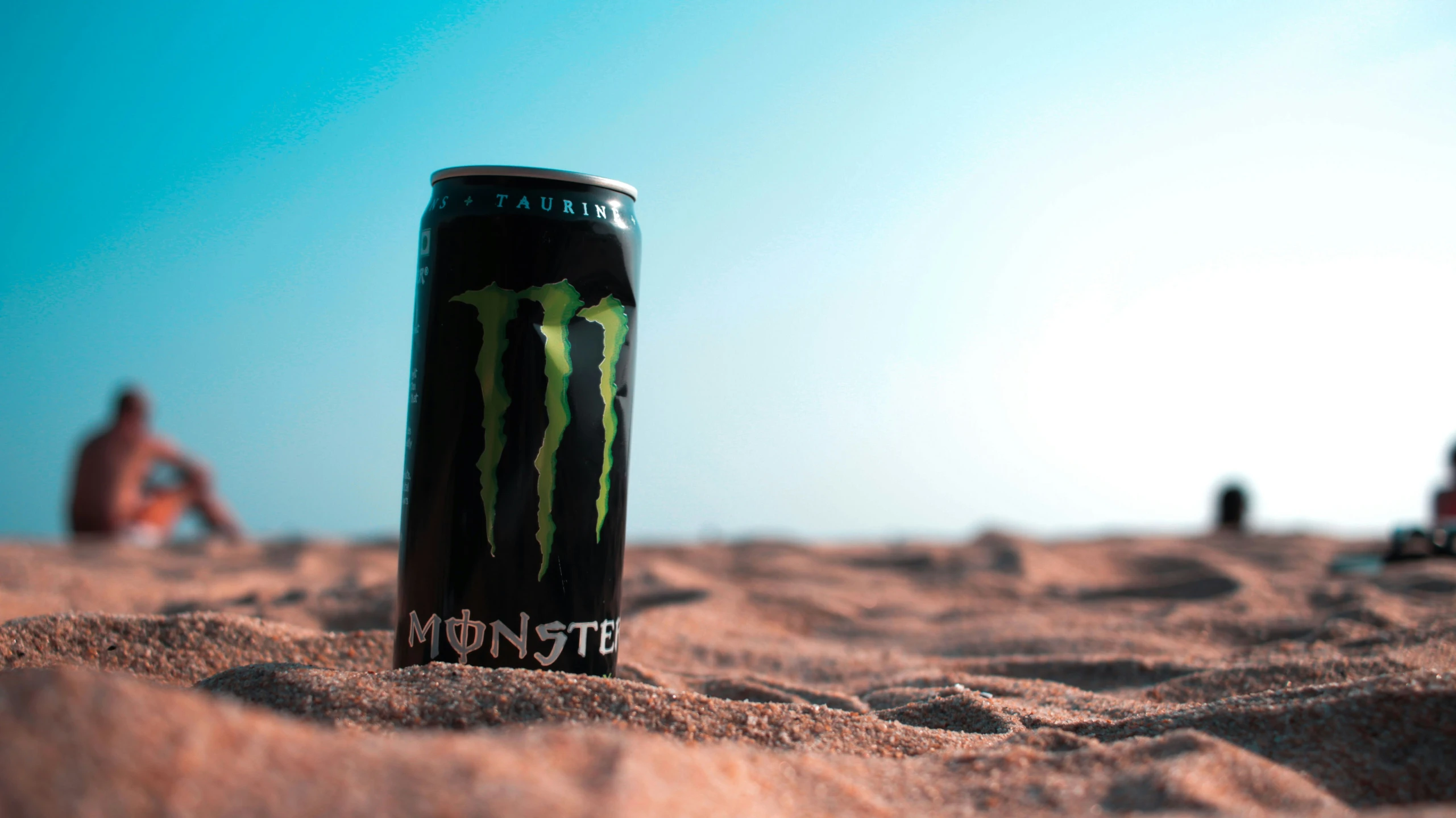 a monster can sitting on sand with people behind it