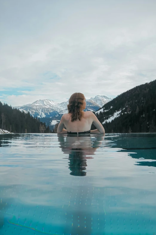 a woman in a one piece swimsuit sits facing mountains