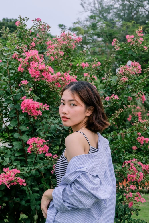 a woman standing in front of a bush with pink flowers