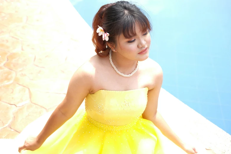 a woman sitting in front of a swimming pool wearing a yellow dress