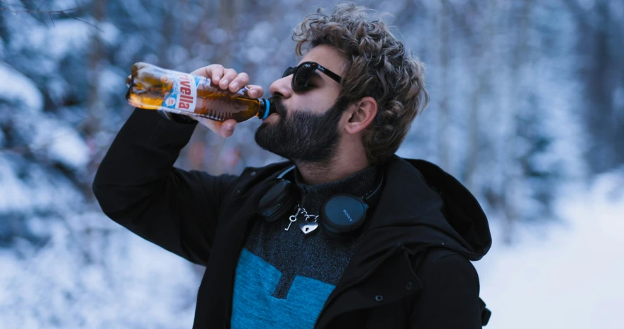 the bearded man in a black jacket is drinking from a can