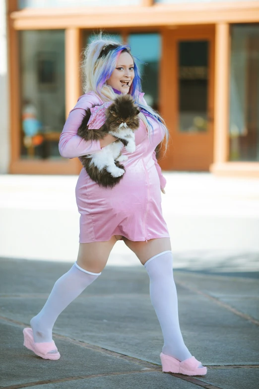 a woman in pink dress walking down street carrying cat