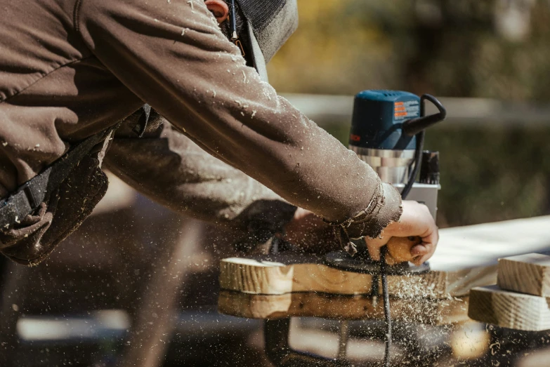 a person holding an electric sander, sanding wooden block ends