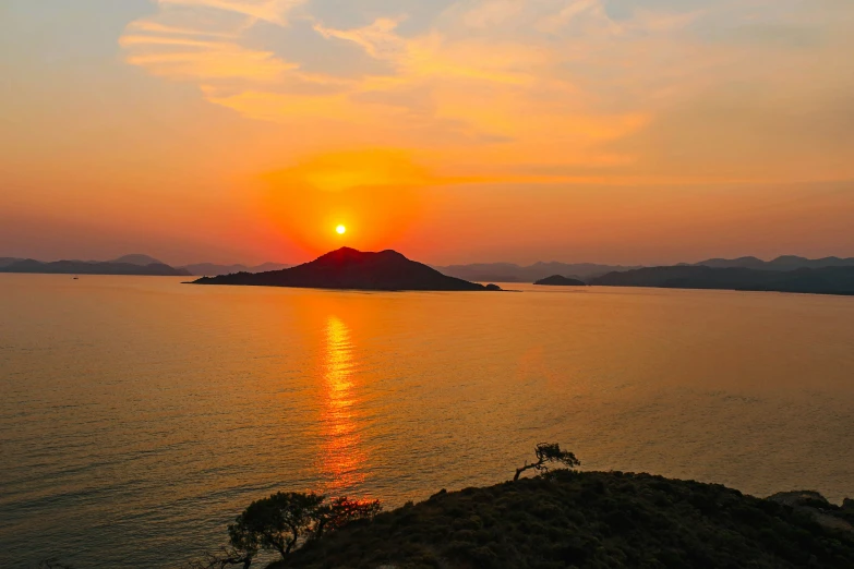 the sun is shining behind a mountain at the water