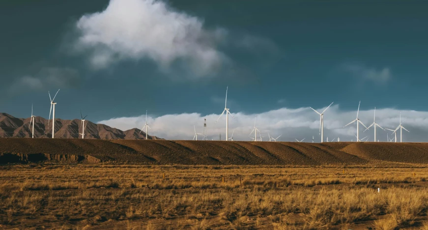 many wind mills in the desert with a cloudy sky