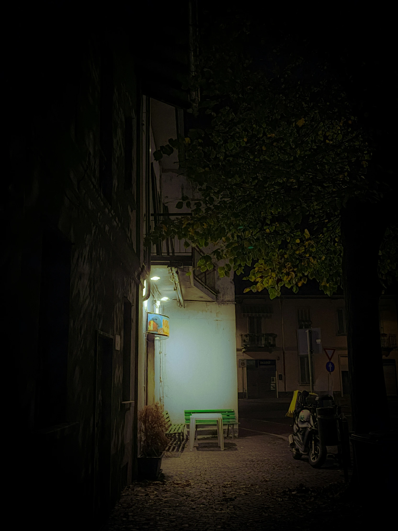 a dark street scene with a green bench and white screen