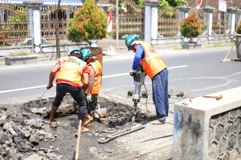 men in orange vests are putting cement into a pit