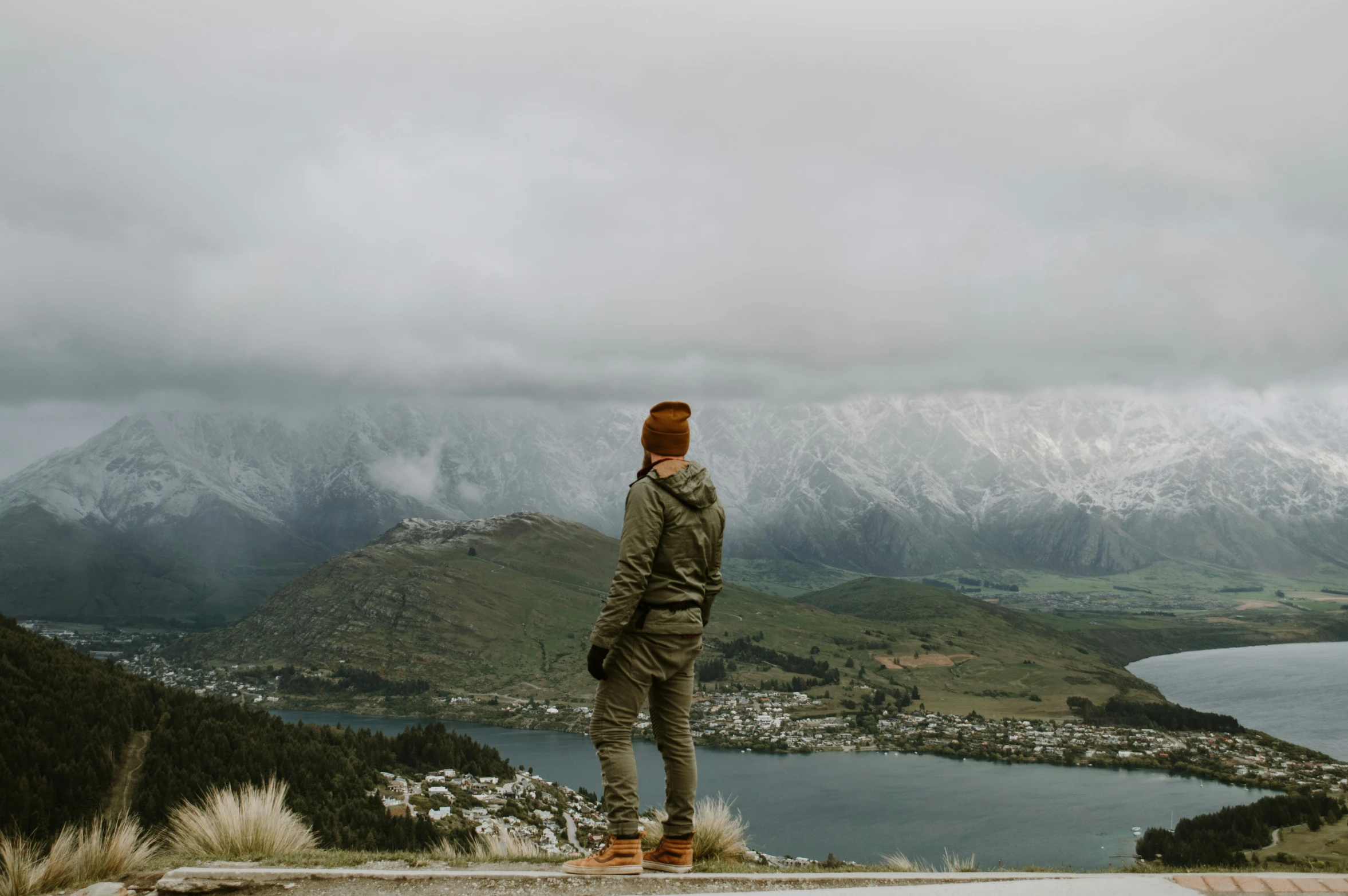 man standing on edge of cliff overlooking lake and mountains