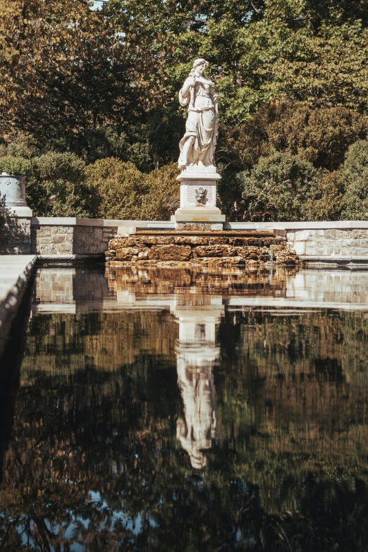 a statue of an angel sits in a pool with water surrounding