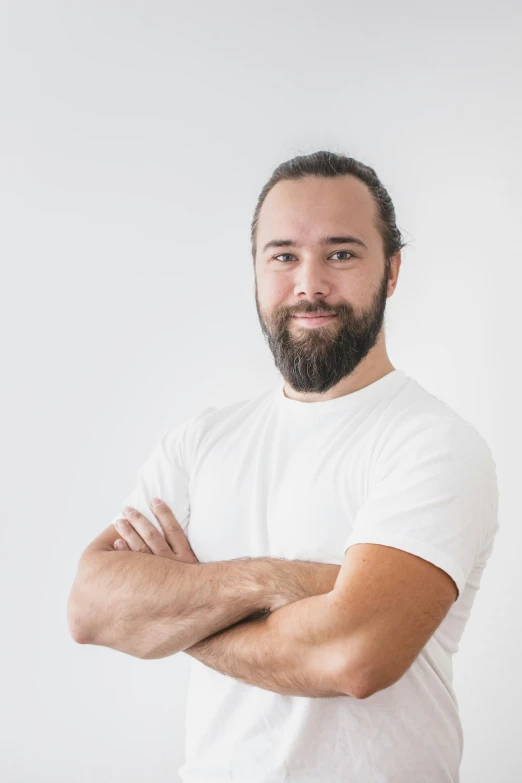 a bearded man with his arms crossed smiling