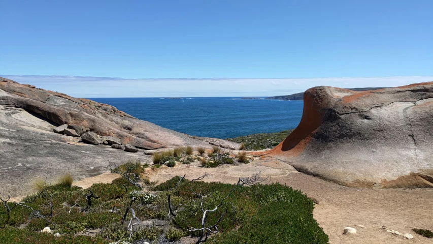 an open area near some water that has green bushes growing on the rocks