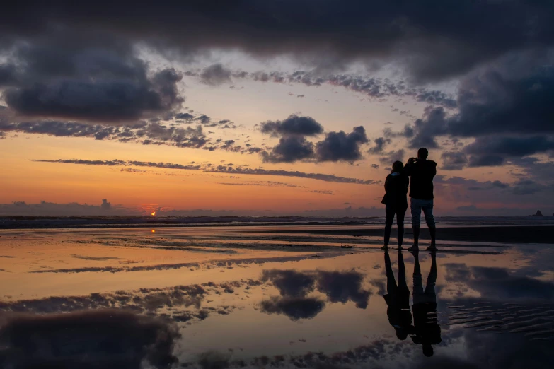 two people looking out to the sunset on a beach