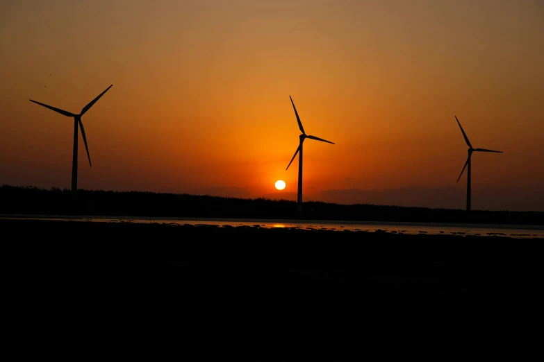 four wind mills in the distance with a setting sun