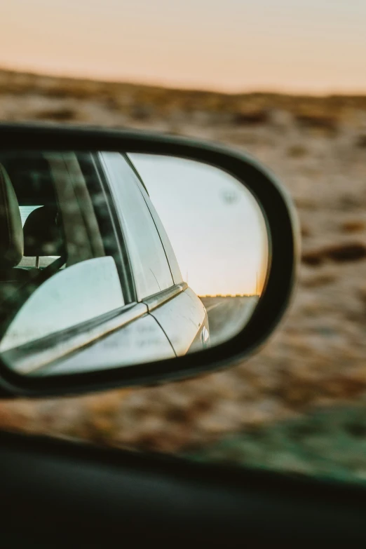 a side mirror on a car that shows the sun