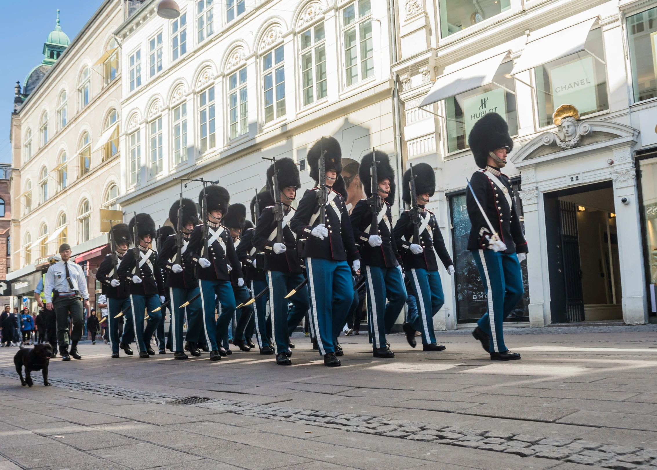 military personnel march down a street near buildings