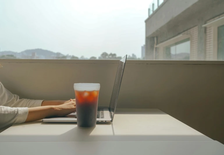 a person uses their laptop and drinks on the table outside