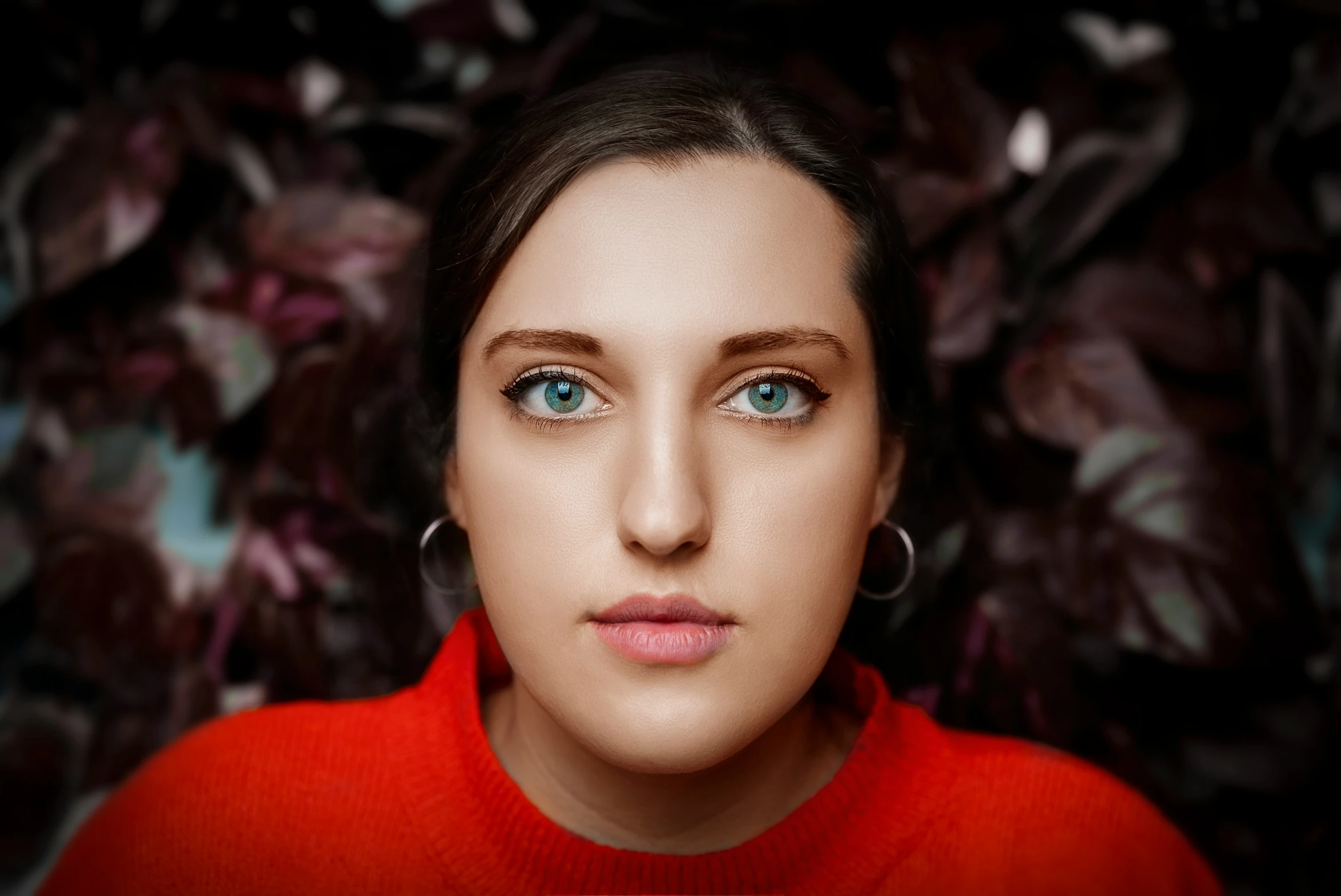 a woman in a red sweater poses in front of flowers