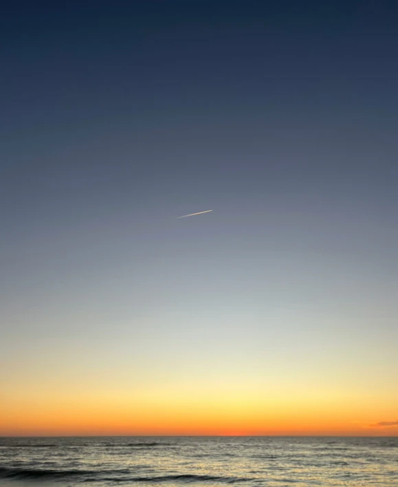 the airplane is flying in the sunset sky above the ocean