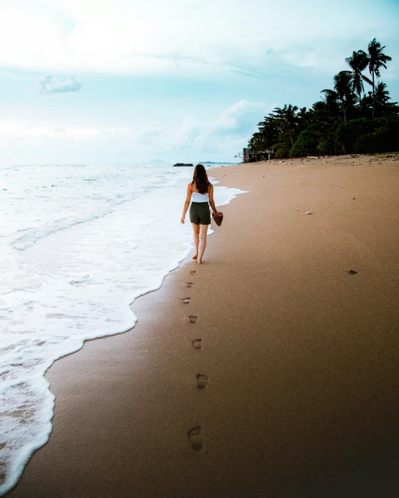 the woman in the dress walks along the shore line towards the water