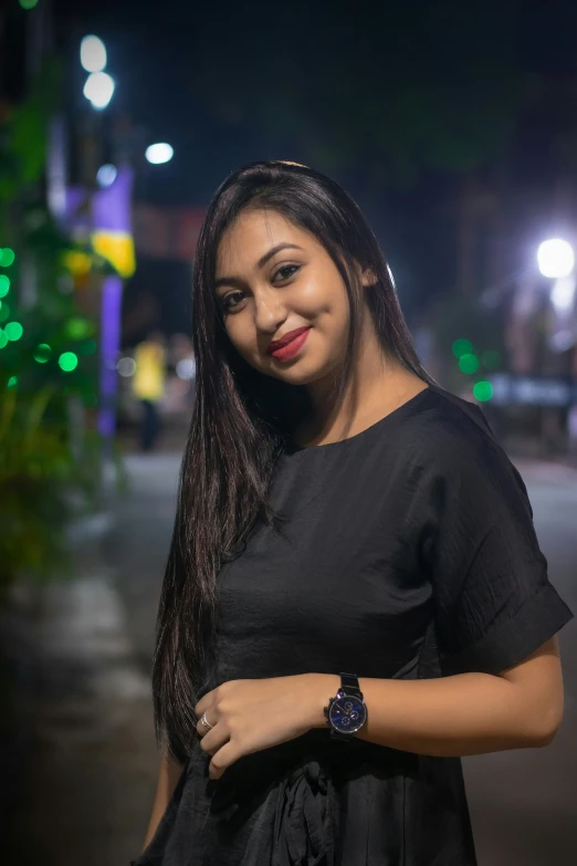 woman in a black dress standing on a street corner at night